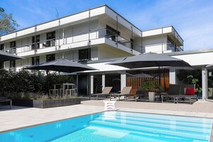 Una piscina al aire libre, sombrillas, sillones reclinables de piscina