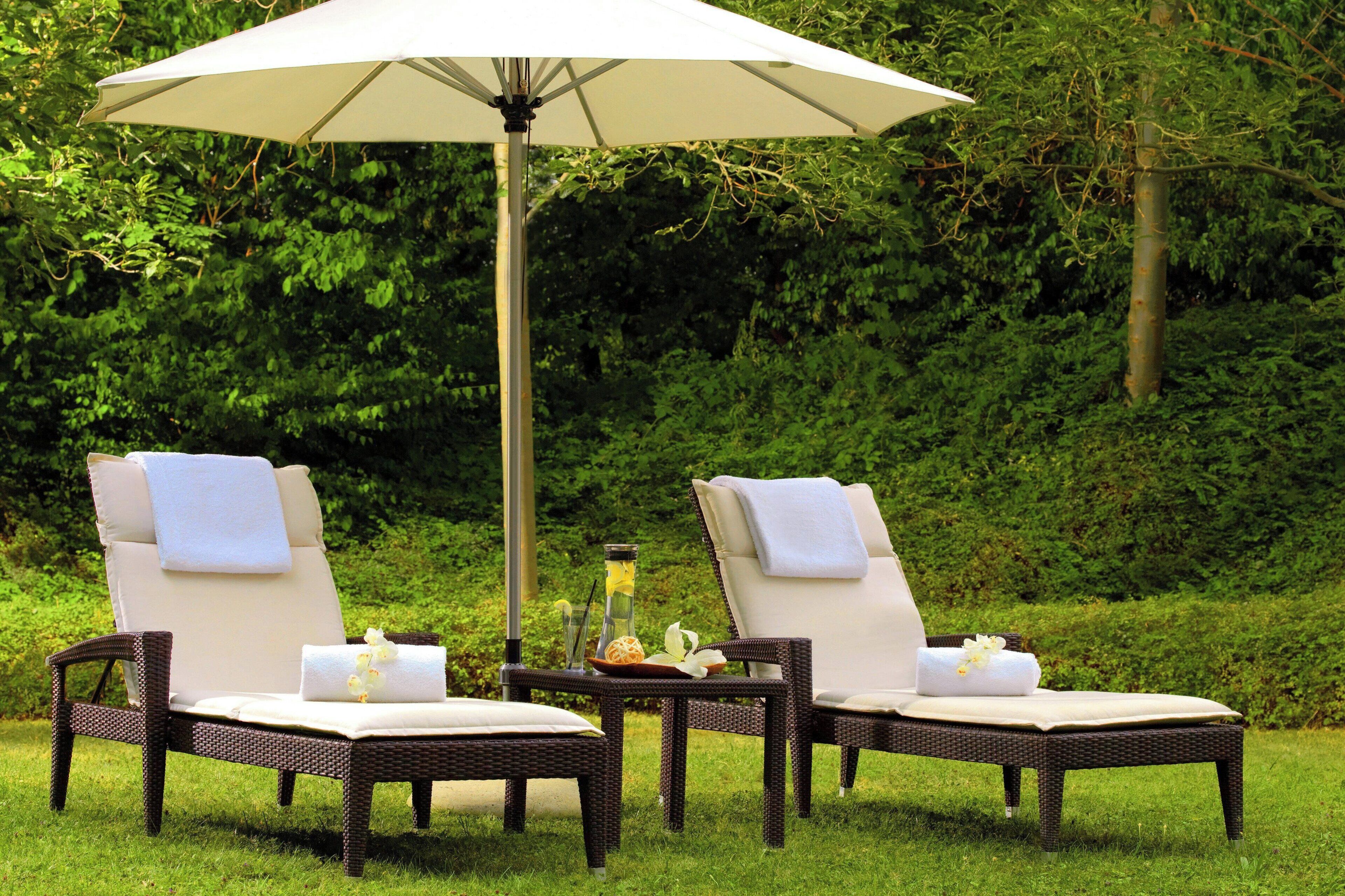 Two wicker lounge chairs with white cushions and towels, an umbrella, and a small table with a bottle and flowers.