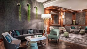 Un moderno vestíbulo de hotel con piso de madera oscura, un sofá gris, una mesa de centro blanca y plantas verdes en la pared.
