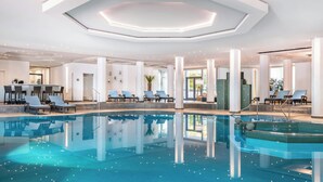 Una piscina interior moderna con agua cristalina, rodeada de sillones de descanso y una zona de bar.