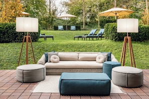 A patio with a sofa, ottomans, and two floor lamps.