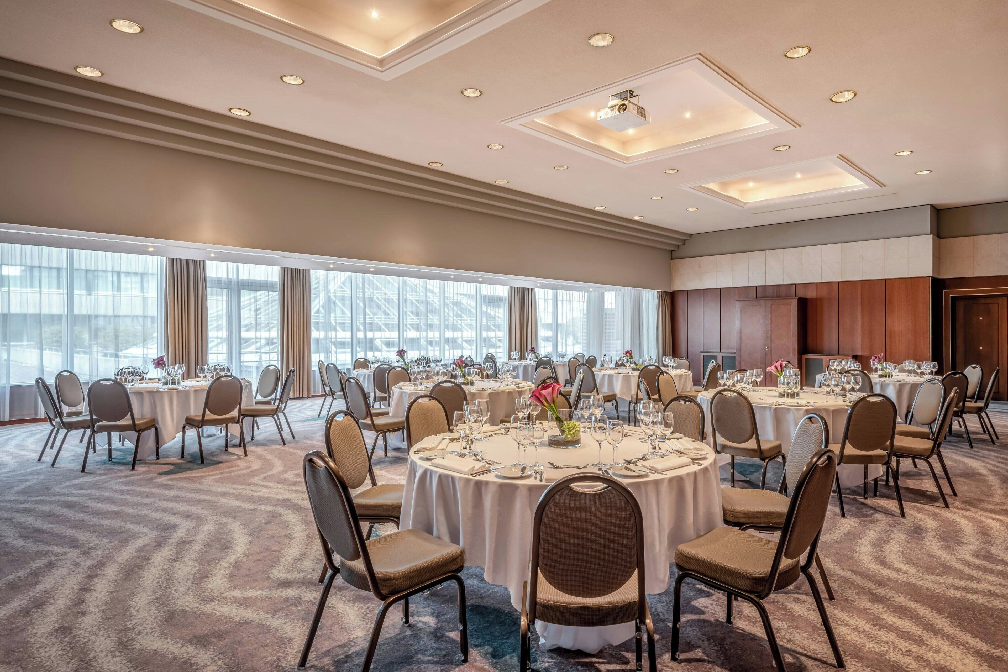 A conference room with round tables, chairs, and a large window with curtains.