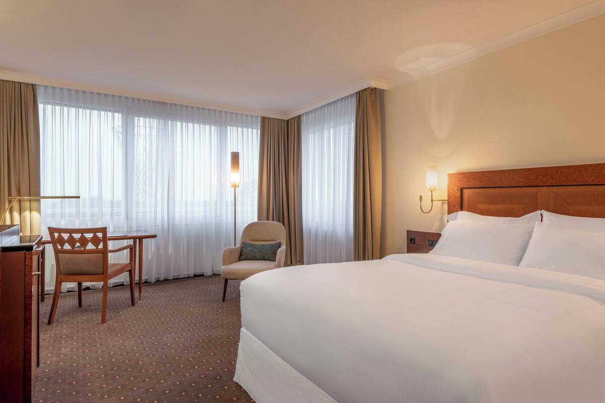 A hotel room with a large bed, a desk with a chair, and a lamp.