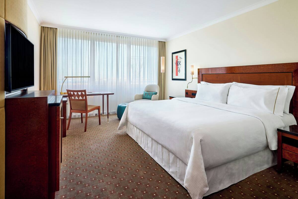 A hotel room with a large bed, a desk with a chair, a television, and a window with curtains.