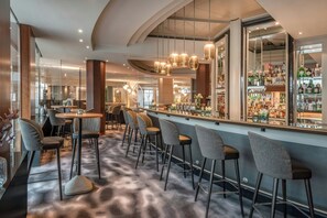 A bar area with high stools and a bar counter, a seating area with round tables and chairs, and a large display of liquor bottles. - The Westin Grand Munich (Munich)