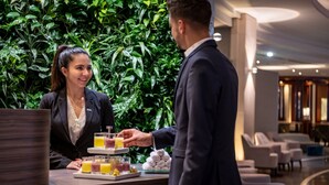 Zona de recepción de un hotel con un muro verde exuberante, un mostrador de recepción y un área de descanso con muebles modernos.