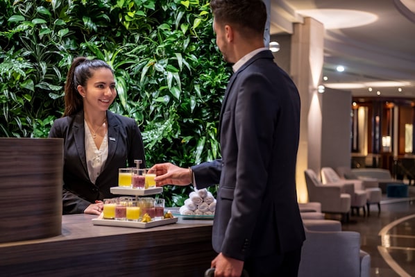 Un espace d’accueil d’hôtel agrémenté d’un mur végétal luxuriant, d’un comptoir de réception et d’un coin salon doté de mobilier moderne.