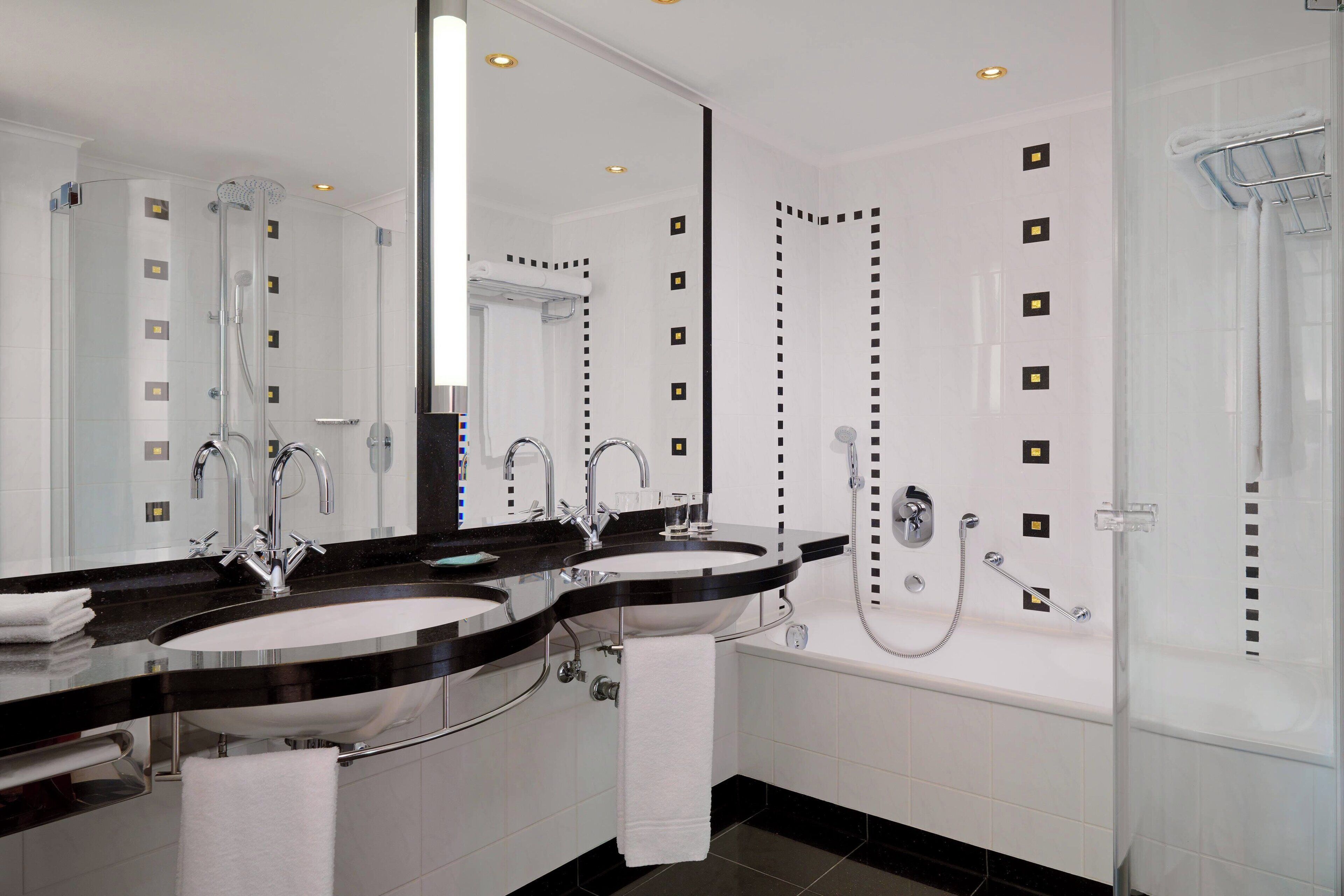 A modern bathroom with two sinks, a large mirror, a bathtub, and a shower.