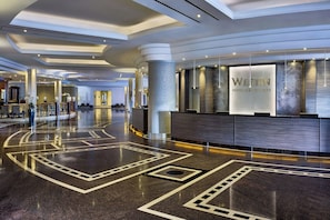 A spacious lobby with a reception desk, a large column, and a polished floor with geometric patterns.