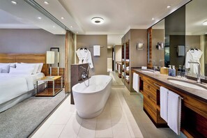 Un baño de hotel moderno con una bañera grande, zona de ducha independiente y tocador con espejo.