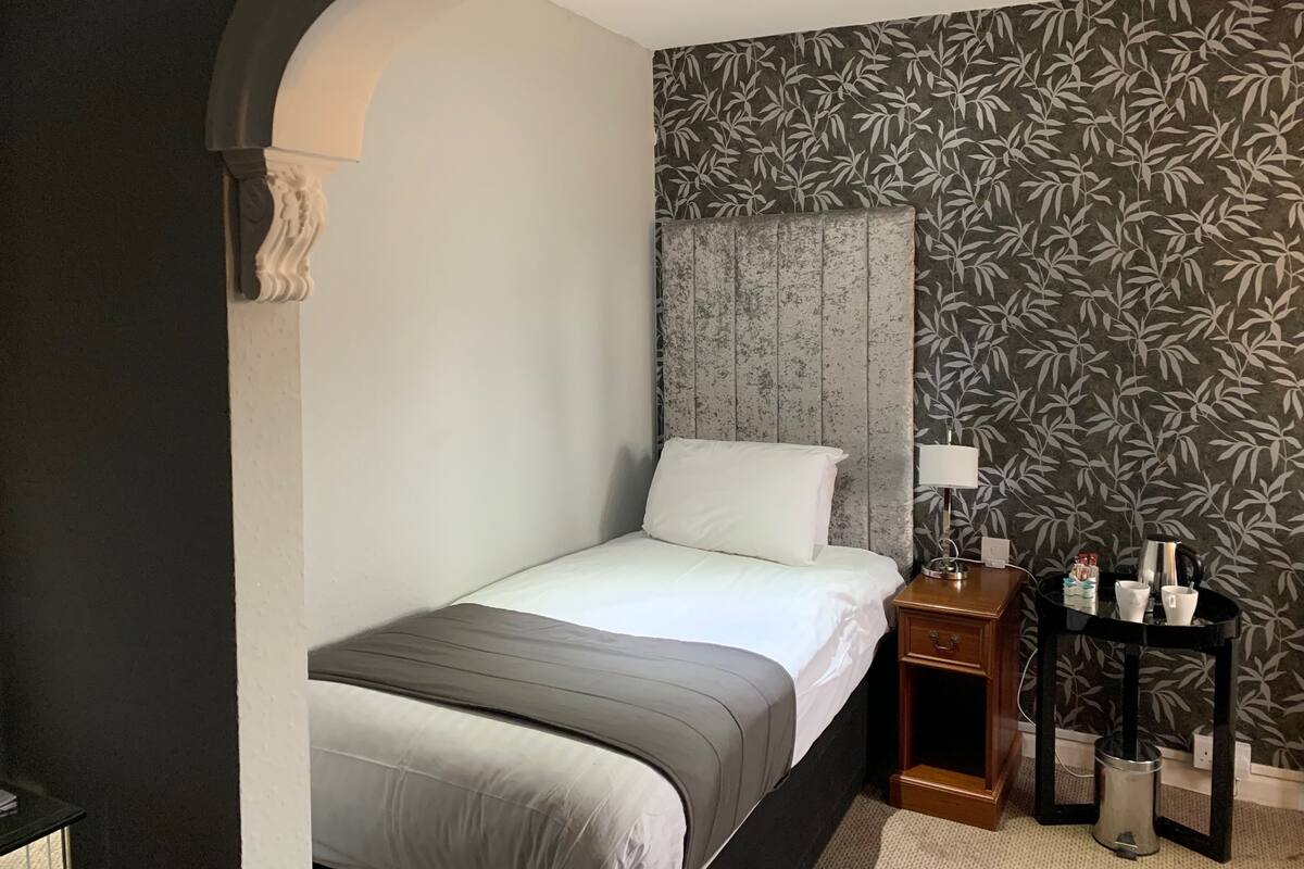 Ein Hotelzimmer mit Bett, Nachttisch, Lampe und einem kleinen Tisch mit Wasserkocher und Tassen.