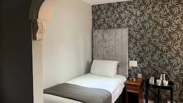 Una habitación de hotel con cama, mesita de noche, lámpara y una pequeña mesa con hervidor y tazas.