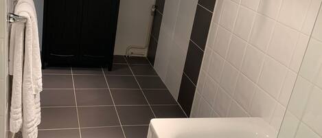 A bathroom with a bathtub, a towel rack with towels, dark and light tiled walls, and a door.