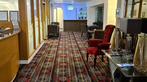Un hall d’hôtel avec un tapis à motifs, un comptoir d’accueil, un espace salon et un bar.