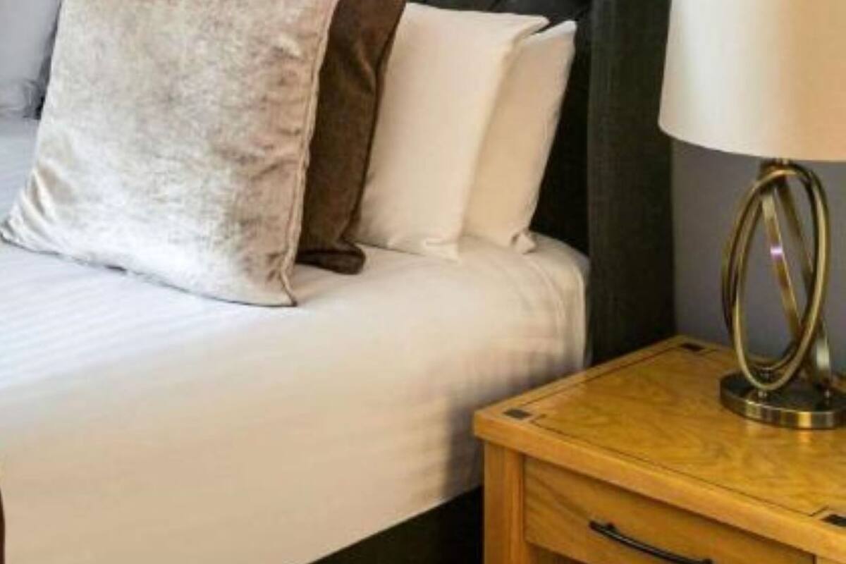Ein Bett mit weißen und braunen Kissen, ein Nachttisch mit Lampe und ein Holzbeistelltisch.