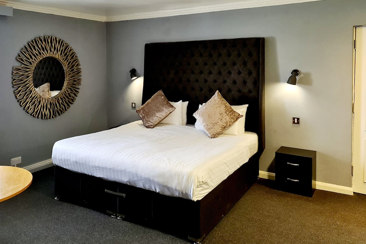 Ein Schlafzimmer mit einem großen Bett, zwei Nachttischen, einem wandmontierten Spiegel und einer Tür.