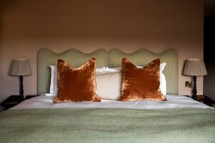 Una cama bien hecha con dos almohadas grandes, un cabecero verde y dos lámparas de noche.