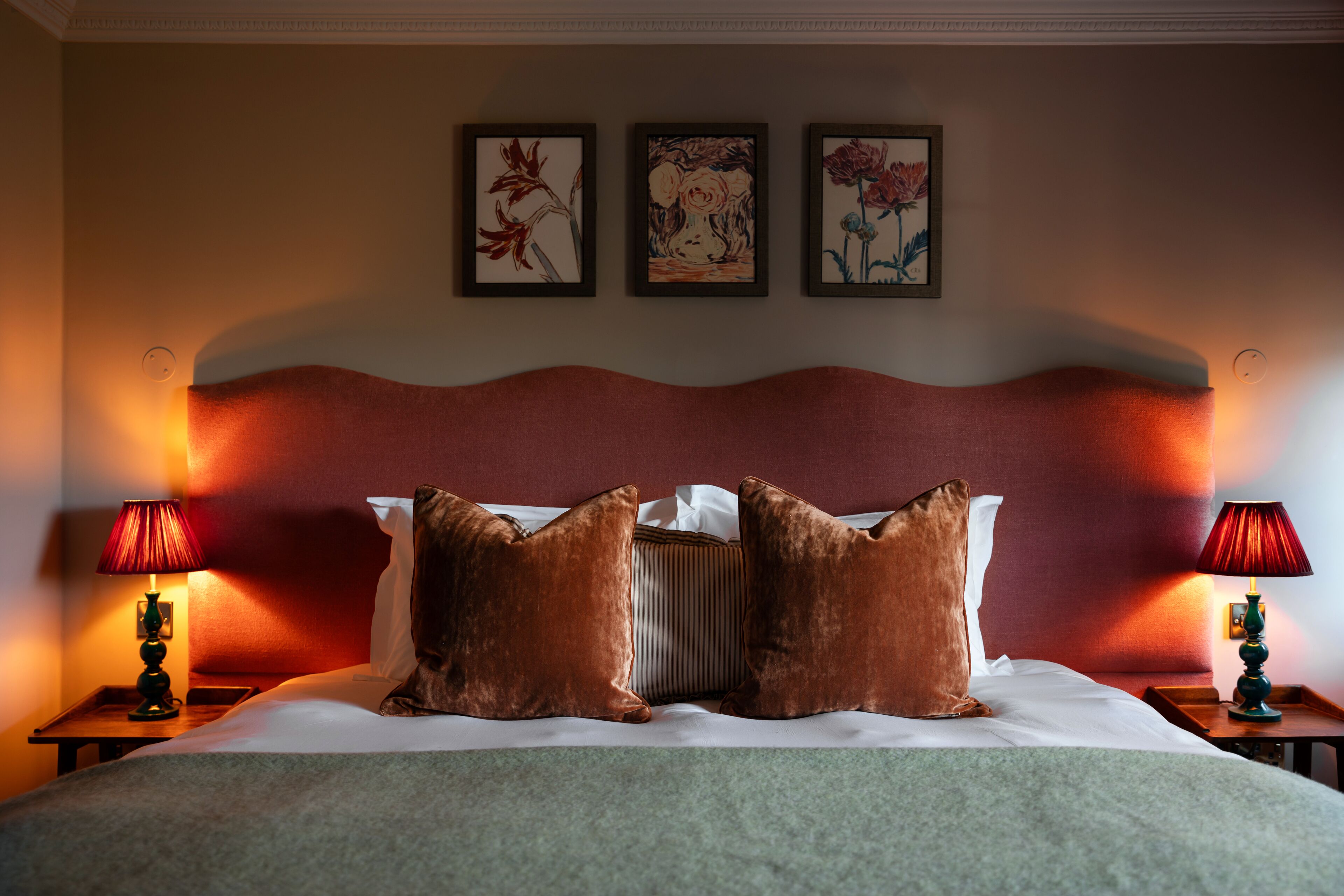 A hotel room with a large bed, two nightstands with lamps, and three framed floral paintings on the wall.