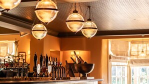 Un espace bar doté de plusieurs tabourets, d’un comptoir avec des robinets et de luminaires suspendus.