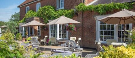 A brick building with a patio area featuring outdoor seating and umbrellas.