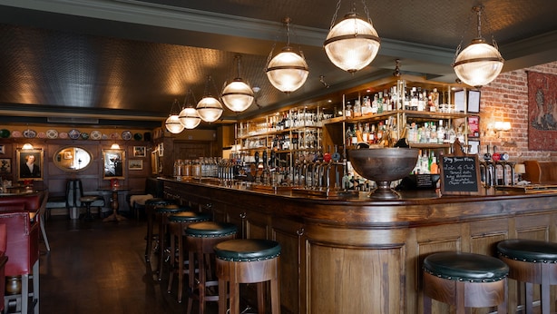 Un espace bar doté de tabourets en bois, de luminaires suspendus et d’un comptoir bien garni.