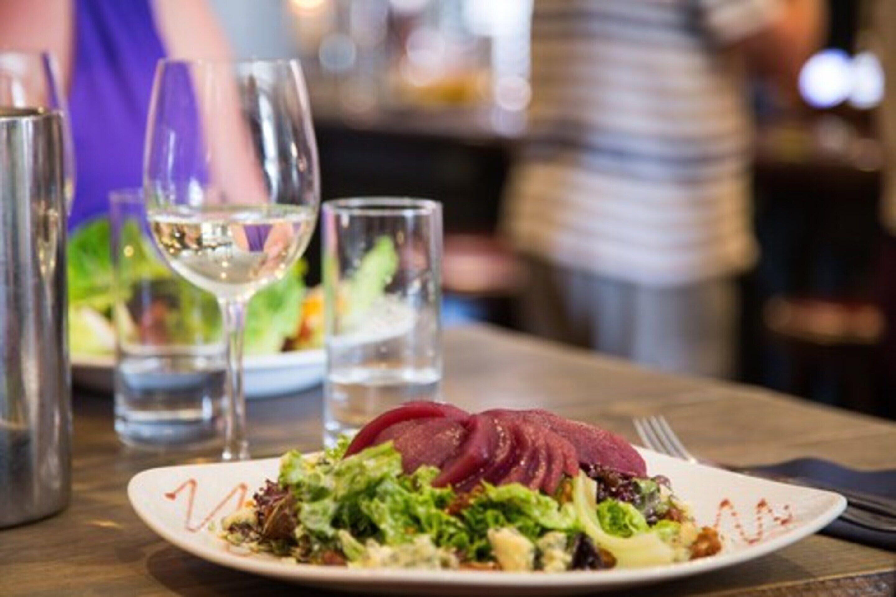 Un plato de comida con ensalada y carne en rodajas, acompañado de una copa de vino blanco.