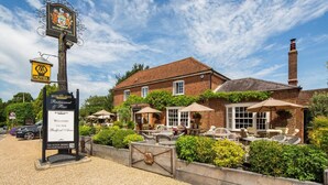 Une demeure de campagne anglaise traditionnelle, avec une enseigne indiquant « Bedford Arms Hotel », et dotée d’une terrasse et d’un jardin.