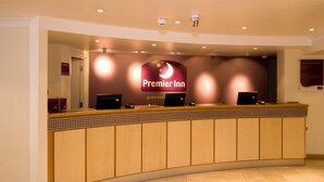 Een receptiebalie van een hotel met een opvallend 'Premier Inn' bord, een betegelde toonbank en een computer.
