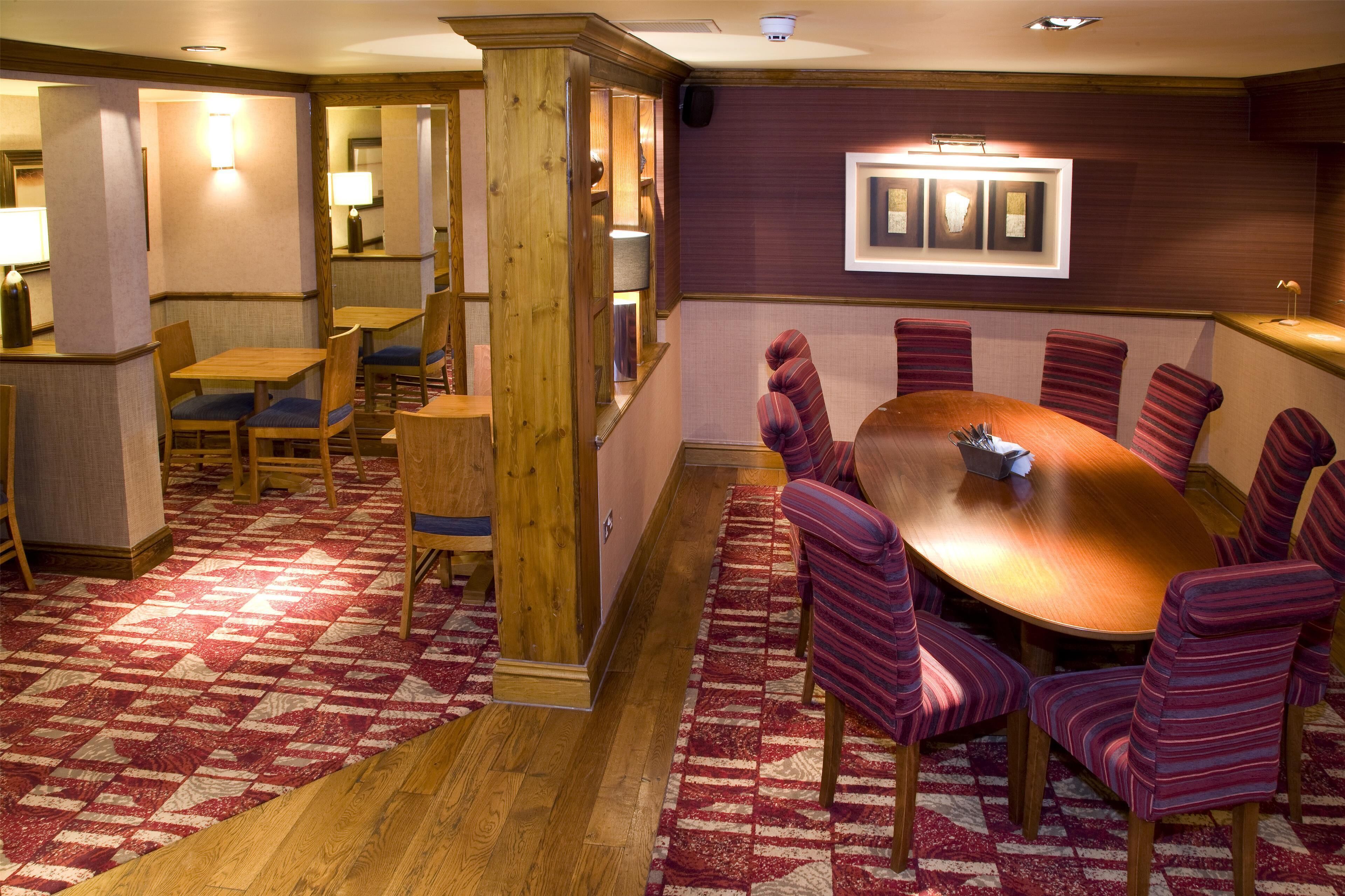 A conference room with a wooden table and striped chairs, a wooden pillar, and a patterned carpet.