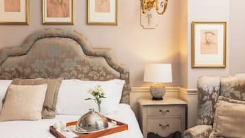 A neatly made bed with a tray, pillows, and a vase of flowers. There are framed pictures on the wall and a lamp on the nightstand.