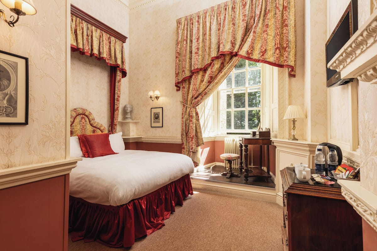 A bedroom with a large bed, a dresser, a vanity, and a window with curtains.