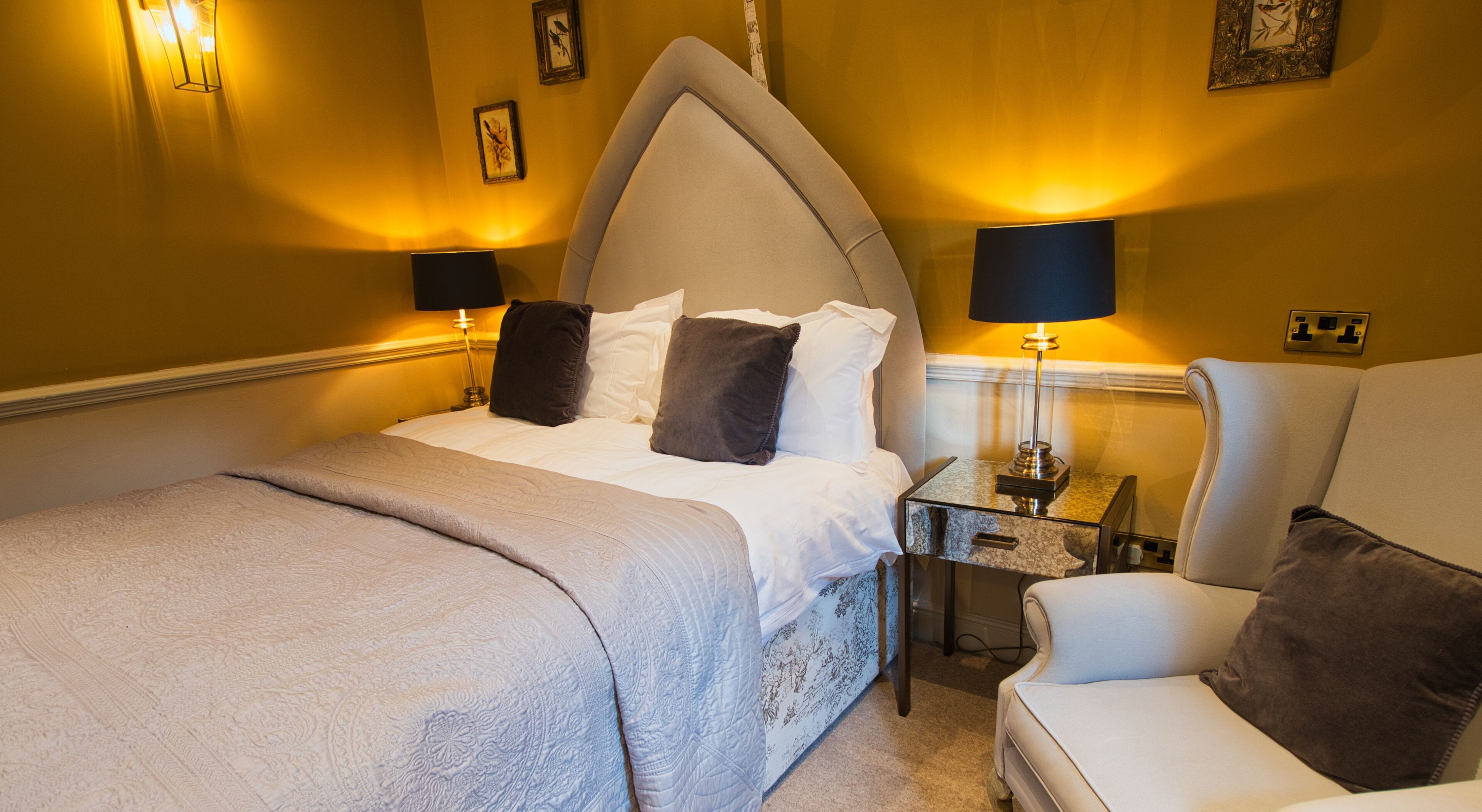 A hotel room with a bed, bedside tables, a chair, and wall-mounted lamps.