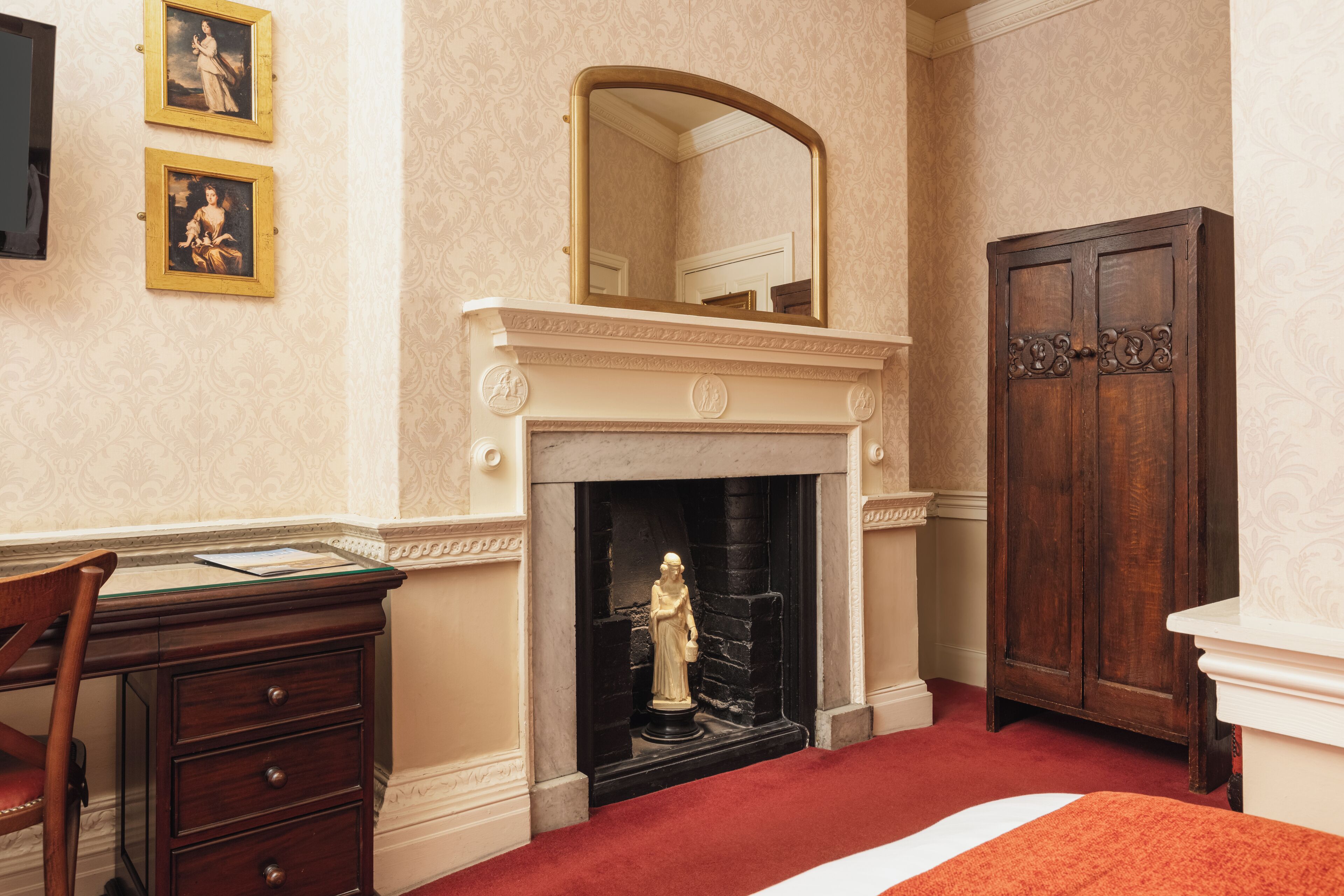 A room with a fireplace, a desk, a chair, and a wardrobe.