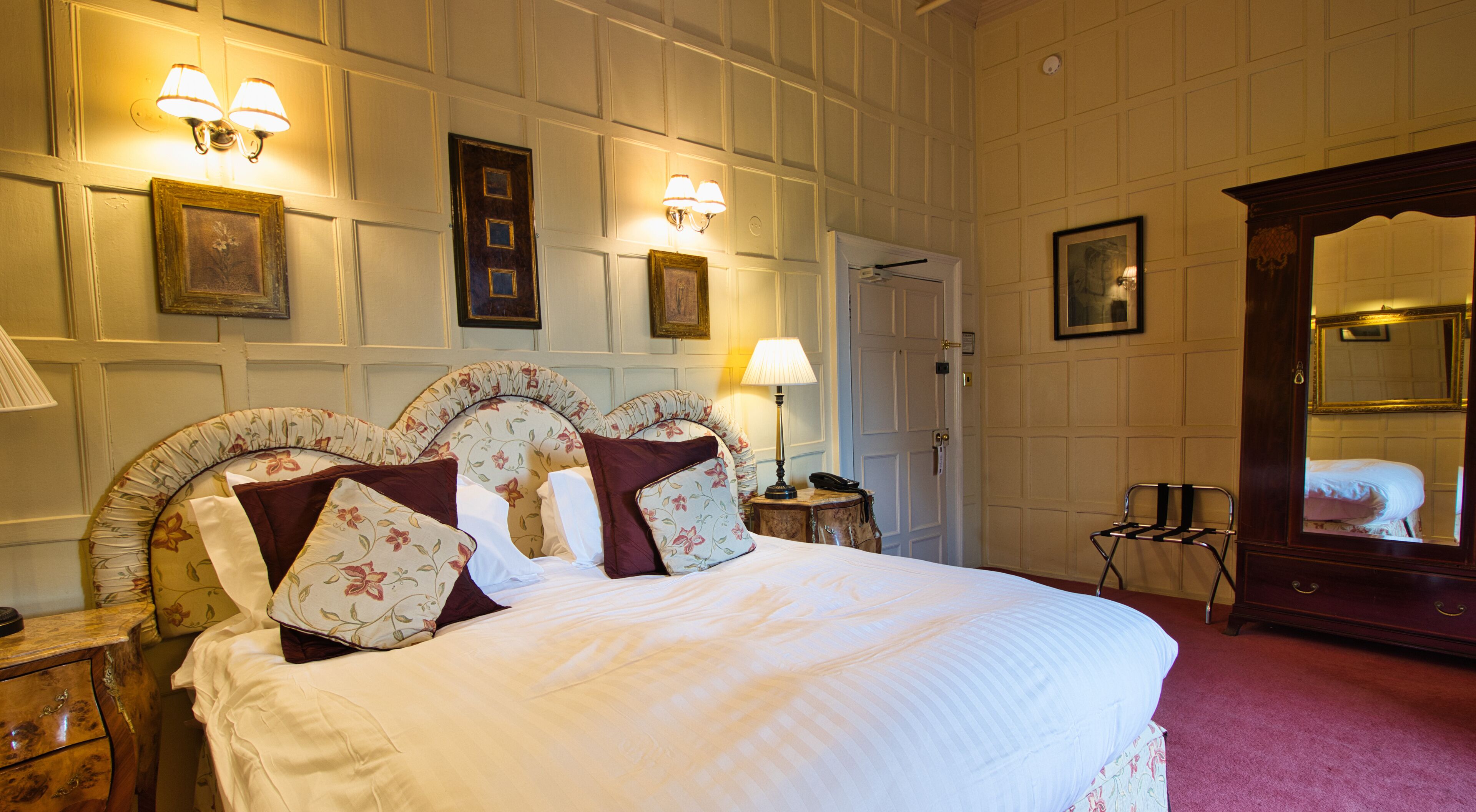 Una habitación de hotel elegante con una cama grande, un tocador, un espejo y lámparas fijadas a la pared.