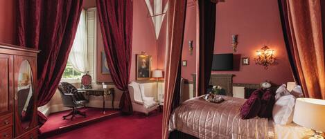 A bedroom with a four-poster bed, a desk with a chair, a mirror, and a fireplace.