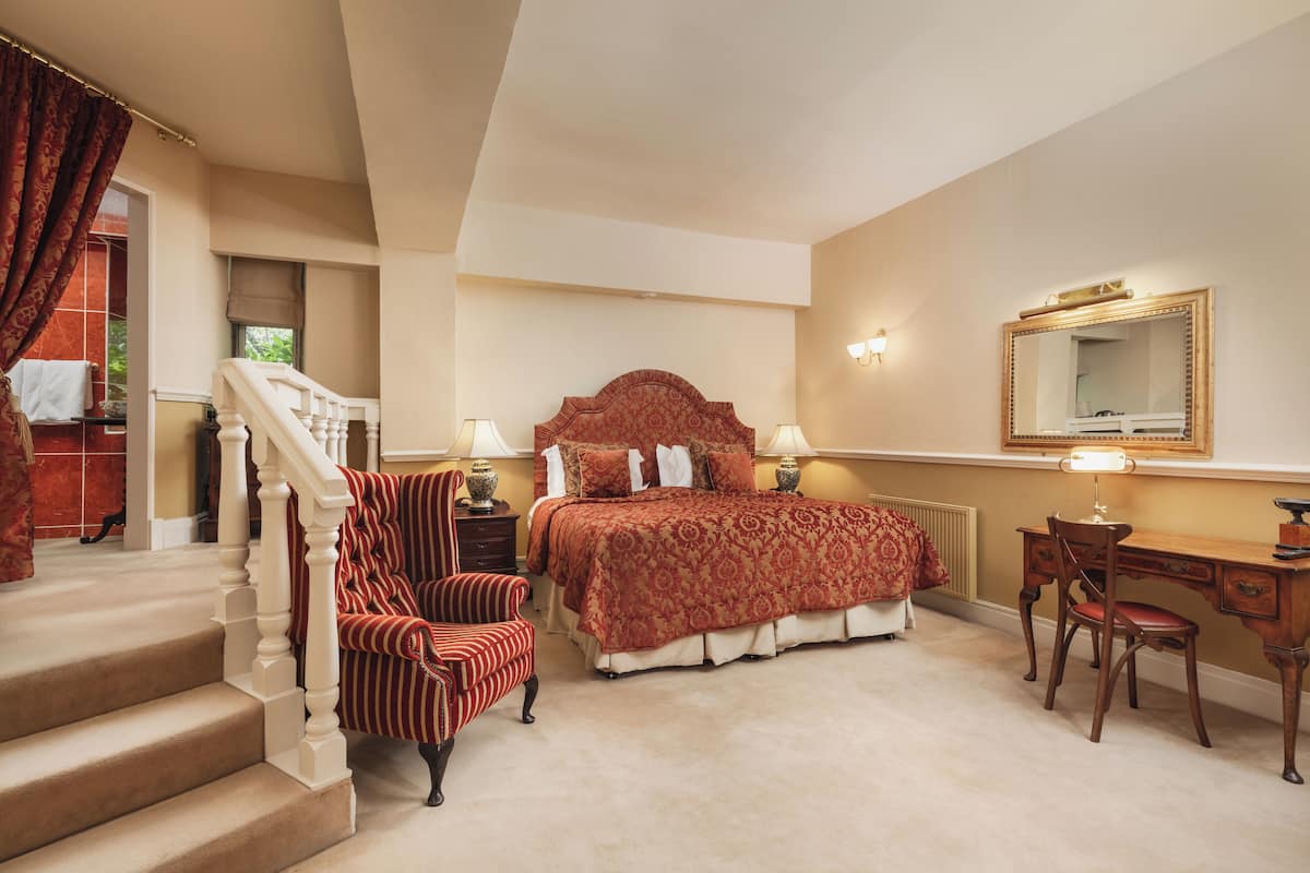 A bedroom with a bed, a desk, a chair, a staircase, and a large mirror.