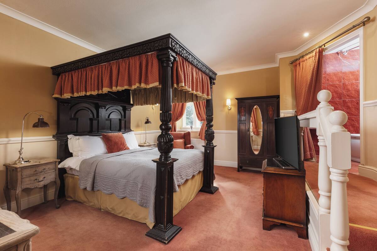 A four-poster bed with a canopy, a wooden nightstand, a dresser, and a mirror.