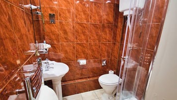 A bathroom with a marble wall, a sink, a toilet, and a glass shower enclosure.