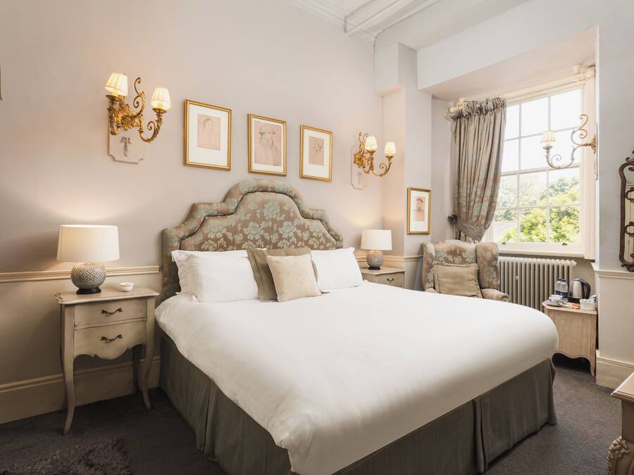 Una cama grande con cabecera floral, dos mesitas de noche con lámparas, y cuadros enmarcados en la pared.