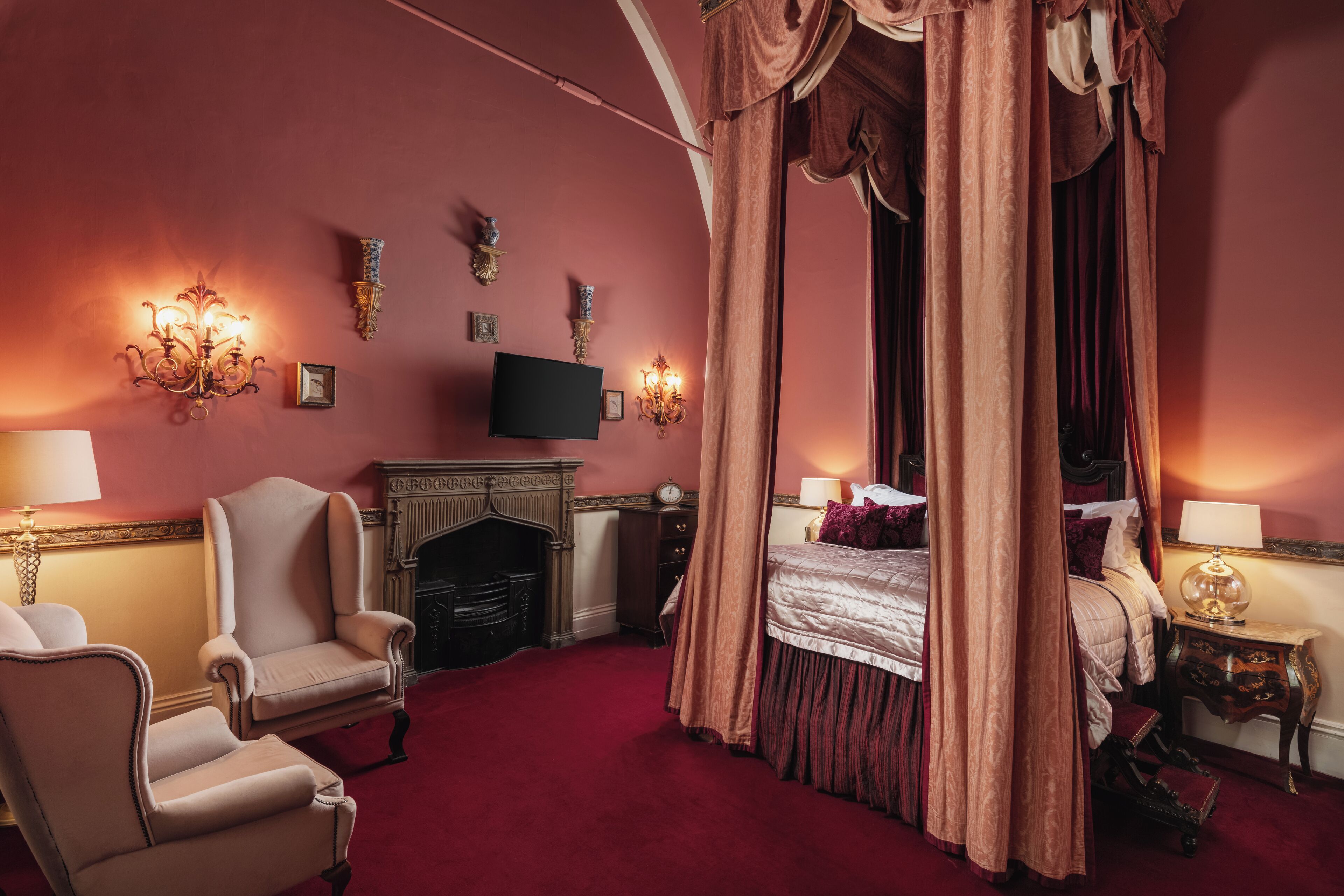 Un dormitorio con cama con dosel, chimenea, televisor y candelabro.