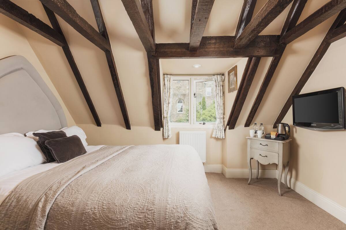 A bedroom with a bed, a nightstand, a television, and a window with curtains.