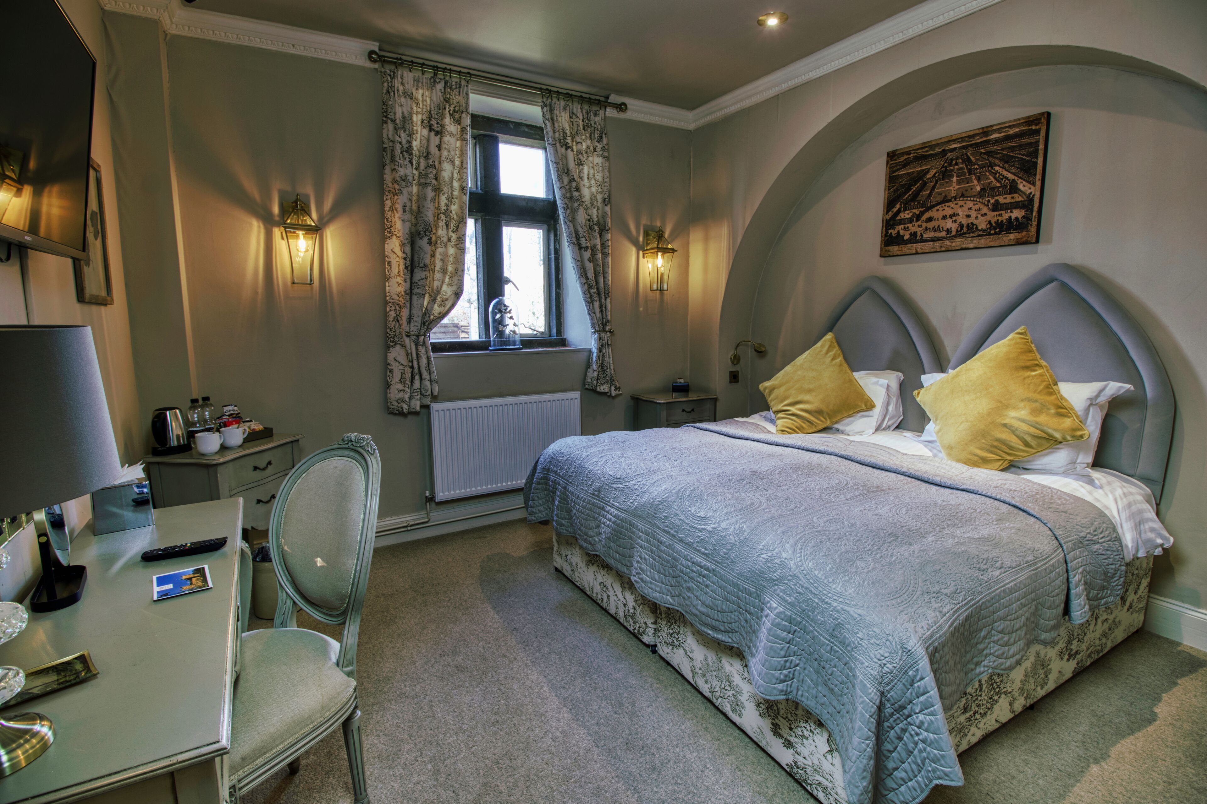 A bedroom with a bed, a desk, a chair, a window with curtains, and wall-mounted lights.