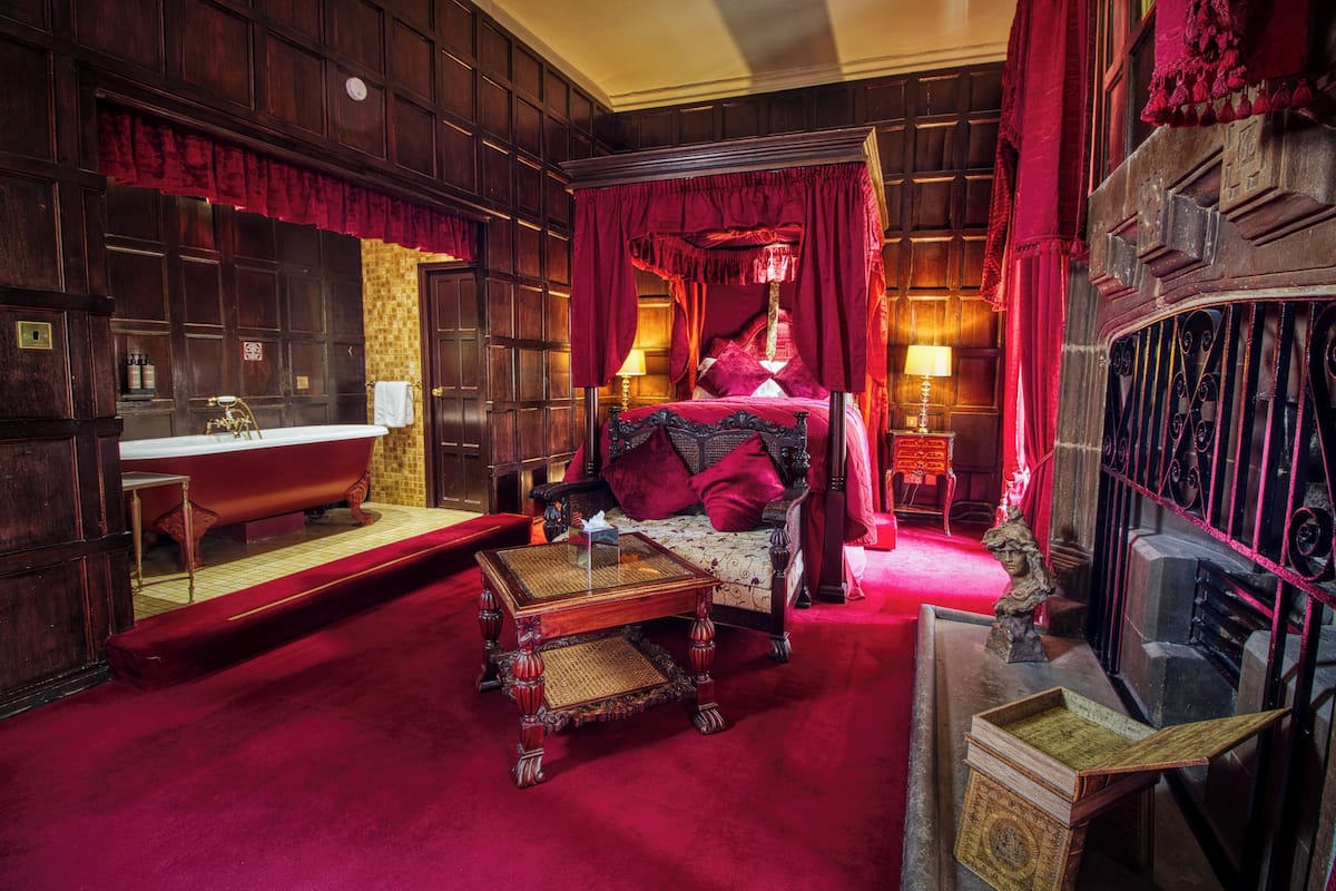 A room with a large bed, a wooden vanity with a mirror, a red carpet, and a red curtain.