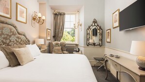 A hotel room with a large bed, a desk, a chair, a radiator, and a window with curtains. - Lumley Castle Hotel (Chester-le-Street)