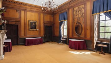 A spacious room with wooden paneling, a chandelier, and large windows with blue curtains.
