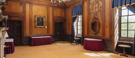 Une pièce spacieuse avec des boiseries, un lustre et de grandes fenêtres ornées de rideaux bleus.