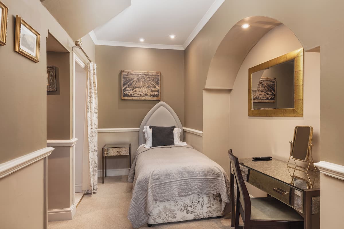 A bedroom with a bed, a desk, a chair, a mirror, and a painting on the wall.