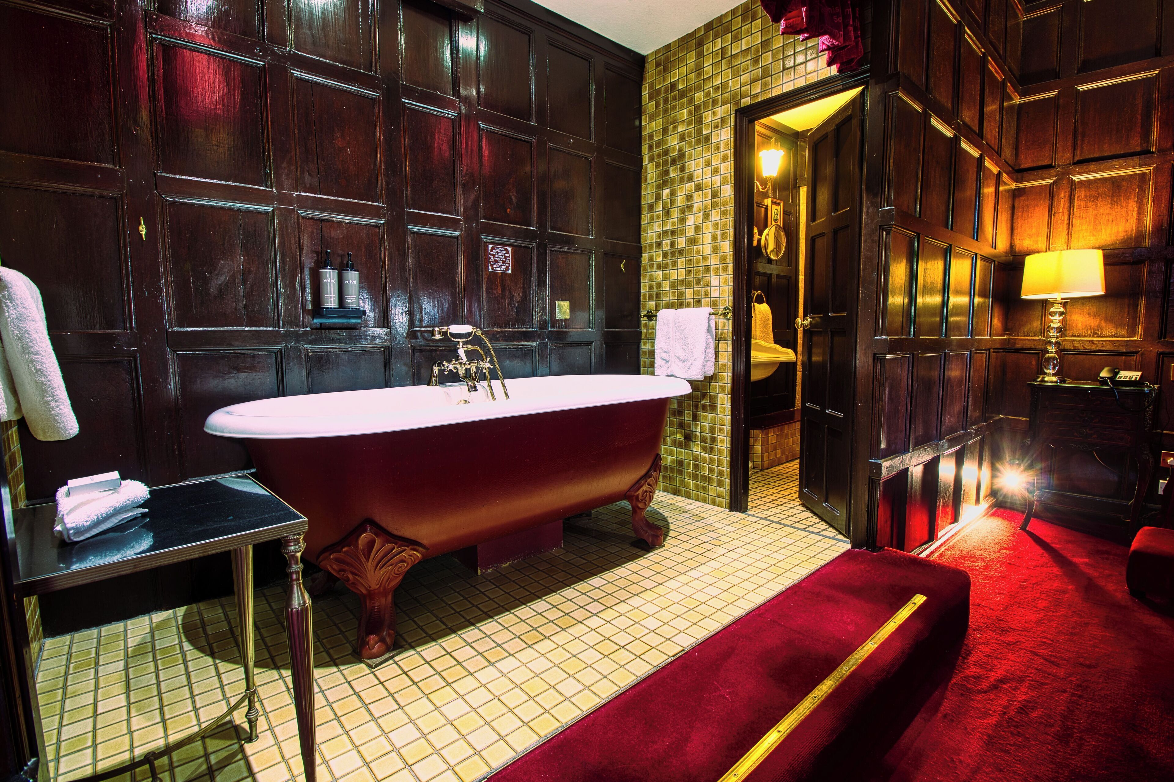 Un baño clásico con una bañera independiente, un tocador con espejo y una zona alfombrada de color rojo.