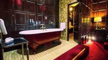 Un baño clásico con una bañera independiente, un tocador con espejo y una zona alfombrada de color rojo.