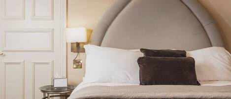 A neatly made bed with a headboard, a bedside table with a lamp, and a framed picture on the wall.